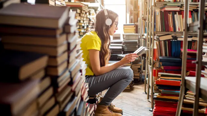 Women listening to headphones and reading book in bookshop